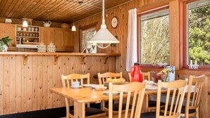 Ein Holzinterieur mit Esstisch, Stühlen, Küchenzeile und Fenster mit Blick auf Bäume.