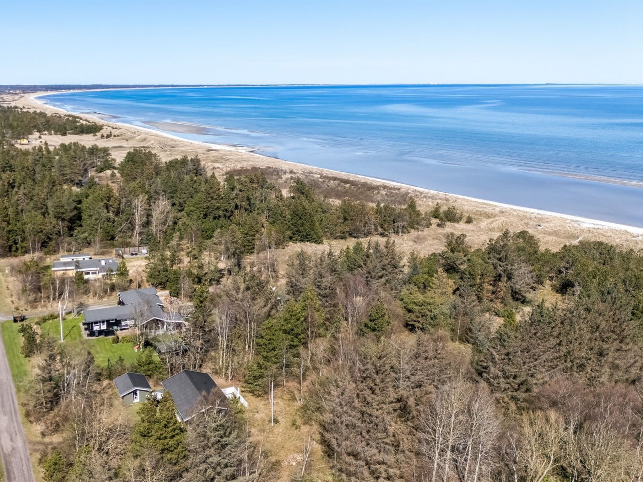 A coastal property with a beach view, dense forest, and a house with a large roof.
