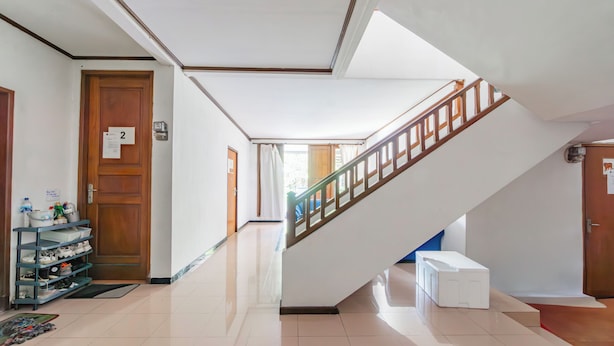Um saguão de hotel com uma porta de madeira marcada '2', um porta-sapatos, uma escada com corrimão de madeira e um banco branco.