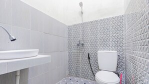 Casa de banho com lavatório branco, sanita e chuveiro. O chão tem um padrão de mosaicos geométricos.