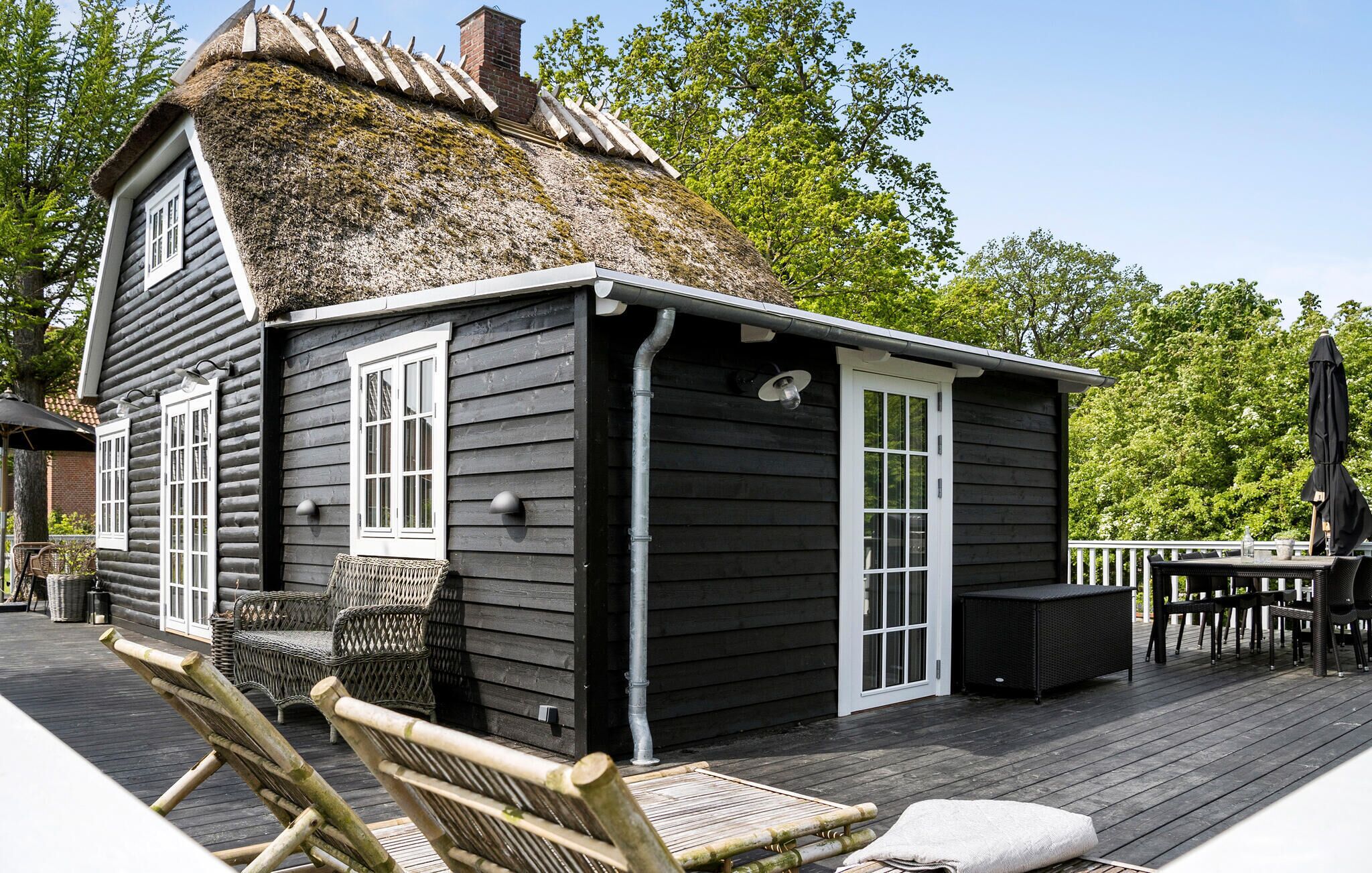 Una cabaña de troncos con techo de paja, una terraza con mobiliario exterior y vistas al follaje circundante.