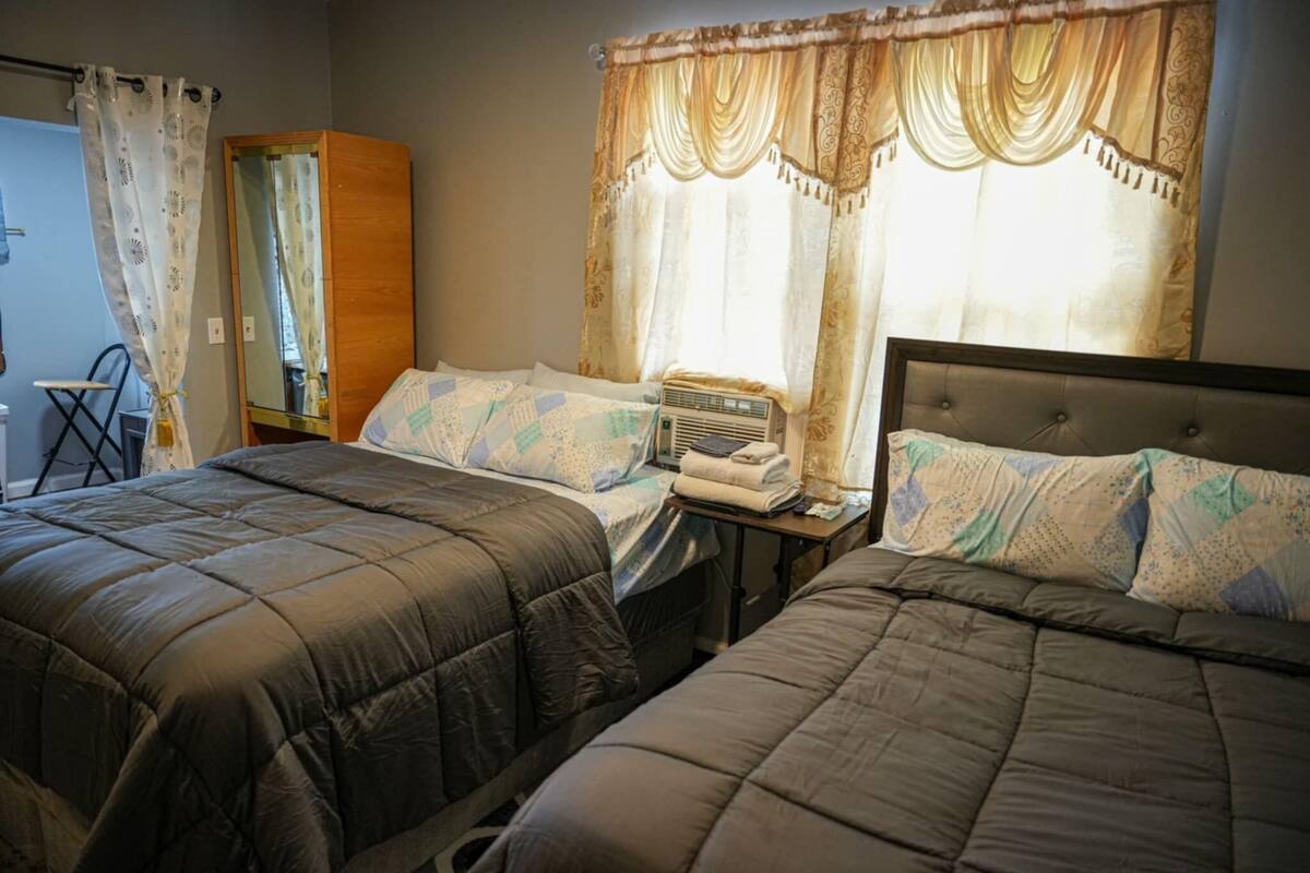 Een slaapkamer met twee bedden, een houten garderobe, een nachtkastje met een lamp en een raam met gordijnen.