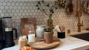 A kitchen with white cabinets, a hexagonal tile backsplash, a coffee maker, a blender, a pitcher, a plant, and a croissant on the counter. - Birds Nest of Topanga - Boho Chic and Minutes from Beach and Topanga Village!! (Topanga)