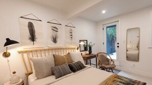 A bedroom with a wooden headboard, a bed with multiple pillows, a bedside table with a lamp, a chair, and a door leading to a balcony. - Birds Nest of Topanga - Boho Chic and Minutes from Beach and Topanga Village!! (Topanga)