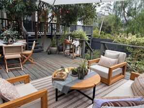 Una terraza de madera con mobiliario exterior, una mesa con una bandeja de aperitivos y plantas en macetas.