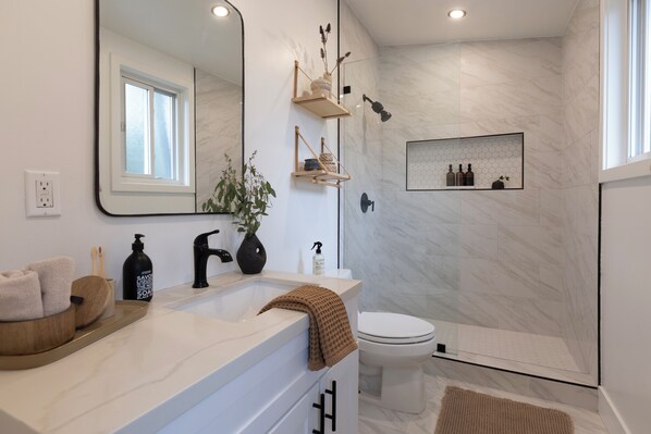 Un baño moderno con lavamanos de mármol blanco, un espejo grande, un inodoro y una zona de ducha.