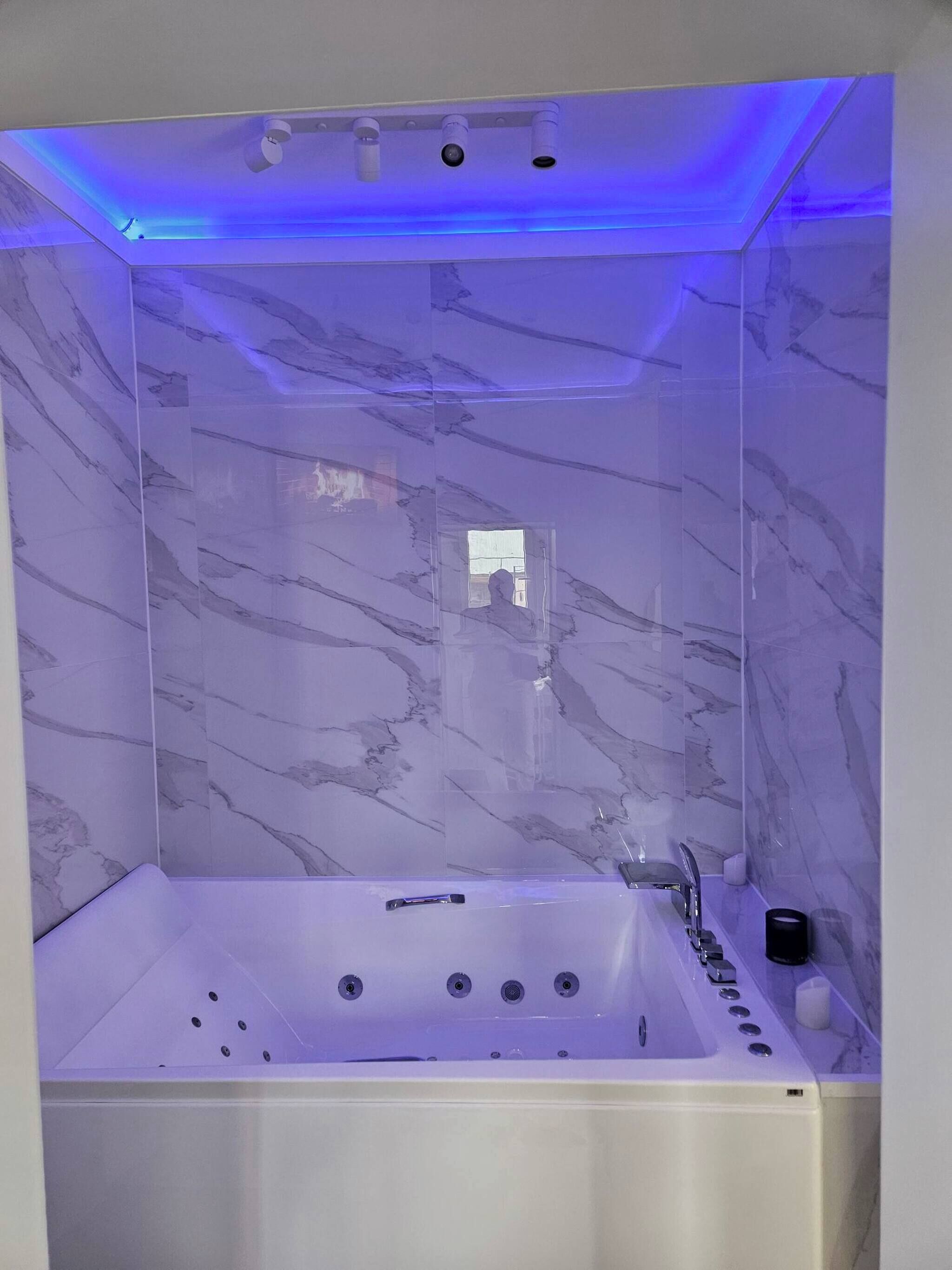 Een moderne badkamer met een marmeren wand, een badkuip en een plafond met blauwe verlichting.