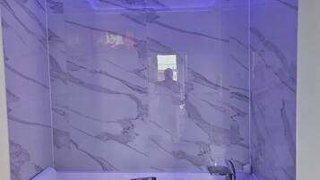 Een moderne badkamer met een marmeren wand, een badkuip en een plafond met blauwe verlichting.