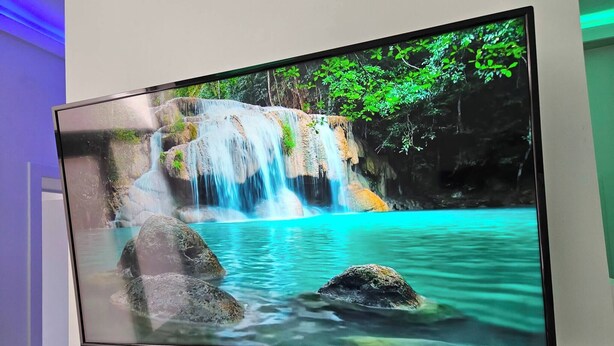 Ein Flachbildfernseher an der Wand zeigt eine Szene mit einem Wasserfall.