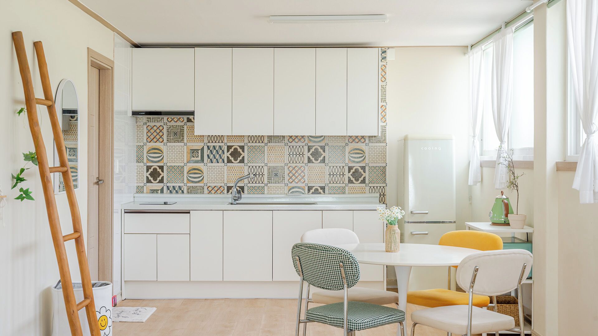 Una cocina compacta con armarios blancos, salpicadero estampado y una zona de comedor con dos sillas.