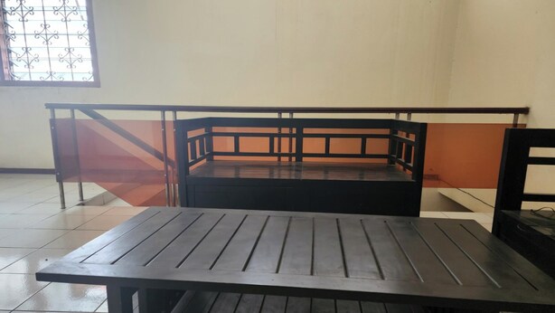 A room with a wooden table and bench, a window with decorative iron bars, and a tiled floor. - OYO Life 93979 Gubeng Homestay Syariah (Surabaya)