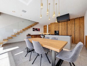 Cocina moderna con armarios de madera, una isla central y un comedor con mesa de madera y sillas grises.