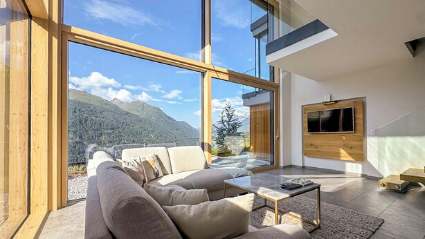 Un salon moderne avec une grande baie vitrée, un canapé, une table basse et un téléviseur fixé au mur.