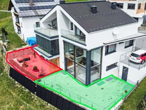 Una casa moderna de dos pisos con techo plano, ventanas amplias y un balcón.