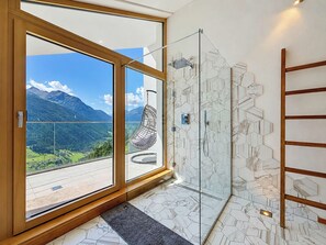 A modern bathroom with a glass shower enclosure, a view of a mountainous landscape, and a hanging chair.