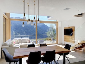 Un interior moderno con comedor, sofá y un amplio ventanal con vistas a la montaña.
