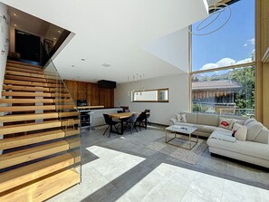 A modern interior with a staircase, dining area, and sofa, featuring a large window with a view of a mountain landscape.