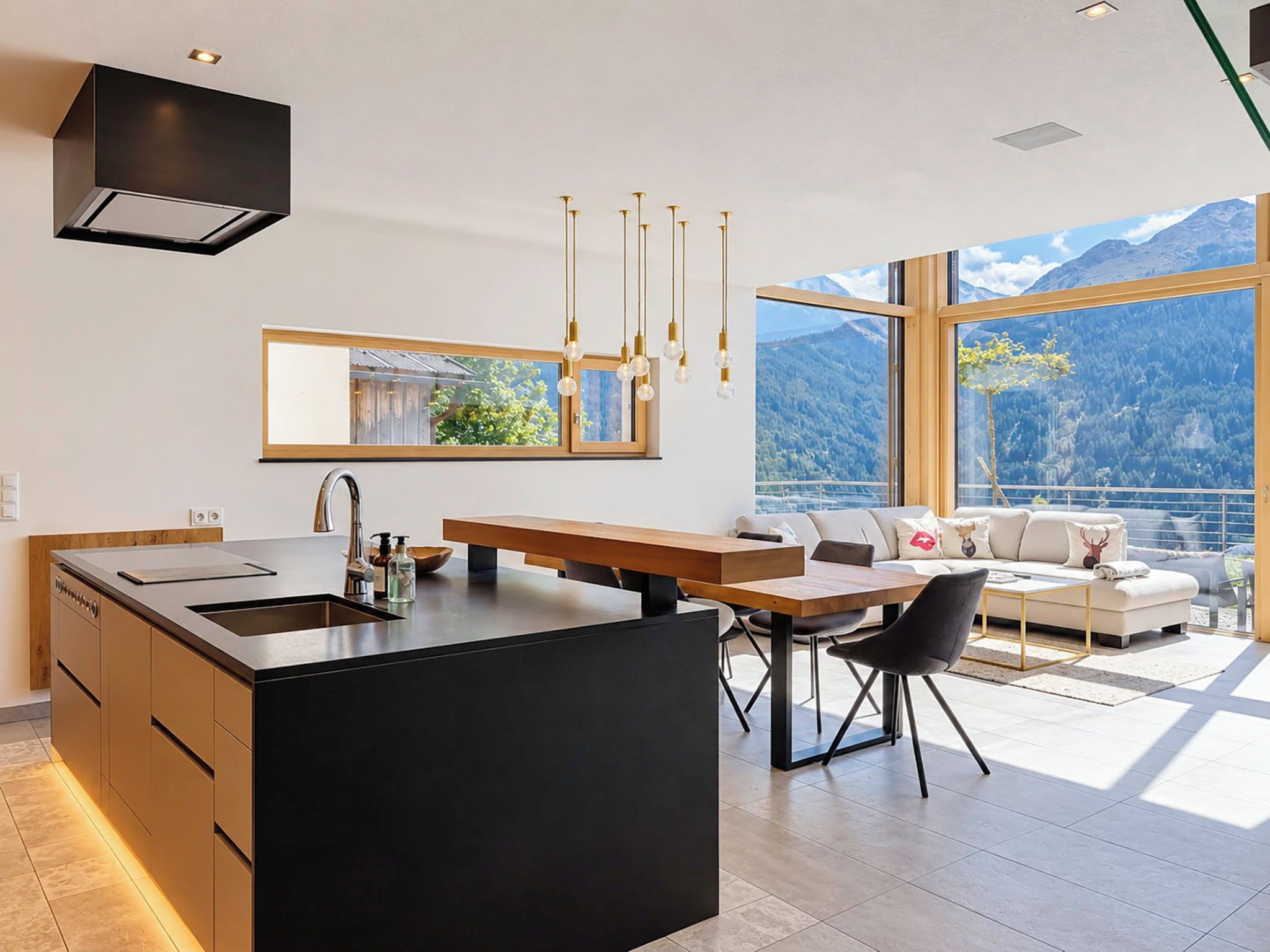 A modern kitchen with a central island, a dining area with a wooden table, and a large window overlooking a mountainous landscape.