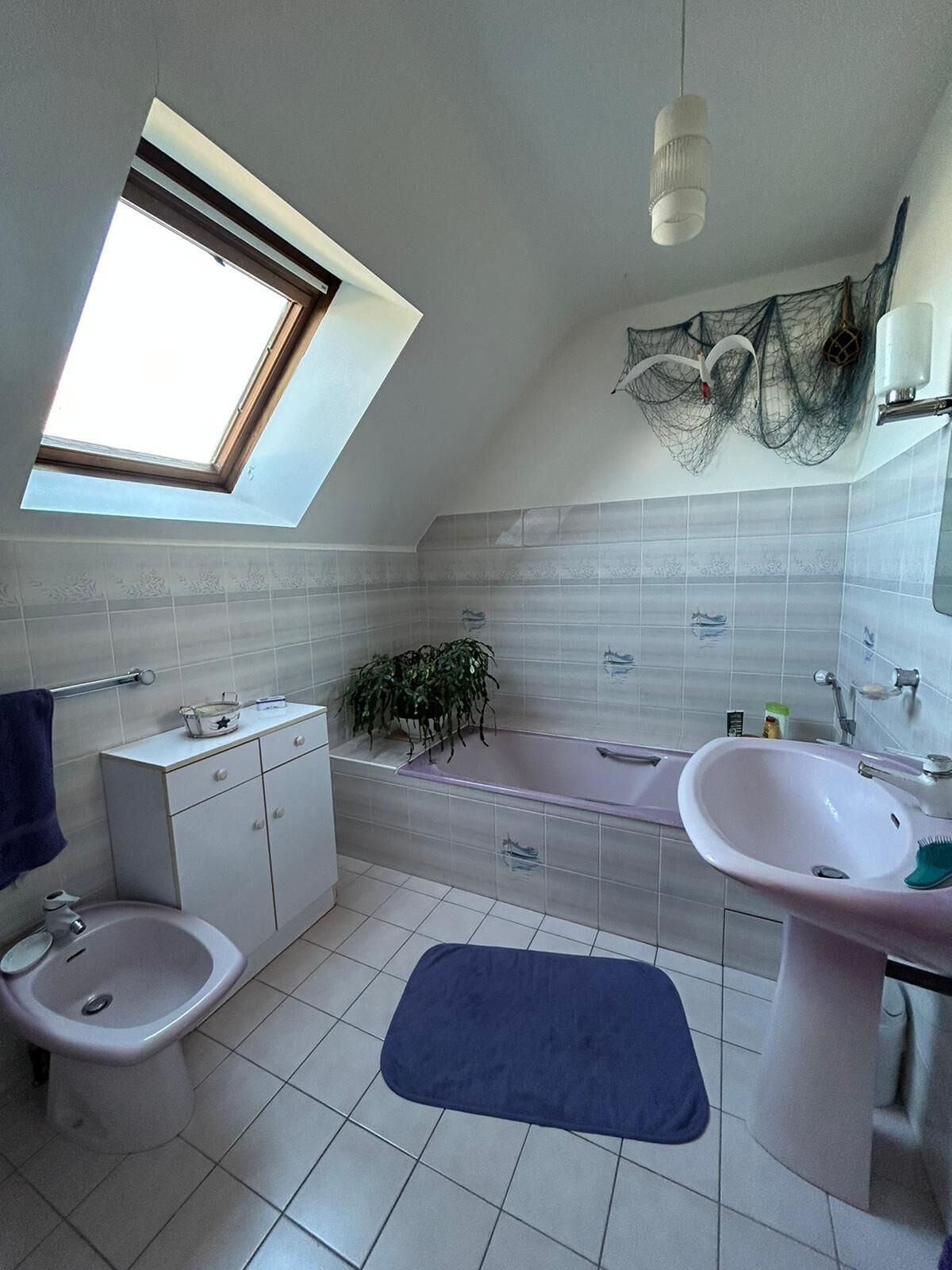 A bathroom with a skylight, a bathtub, a sink, a toilet, and a small plant.
