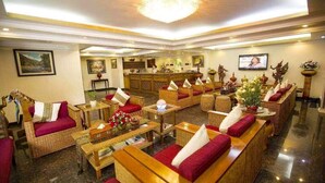 A hotel lobby with wicker furniture, red cushions, a reception desk, and a television screen. - My Hotel Myanmar (Yangon)