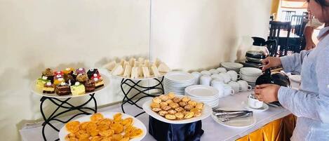 Una mesa con mantel amarillo presenta una barra de buffet con diversos alimentos, incluyendo postres y aperitivos.