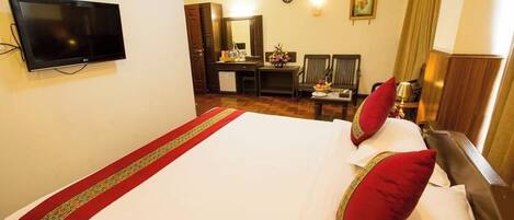 A hotel room with a large bed, a flat-screen TV mounted on the wall, a desk with a chair, and a dining table with chairs.