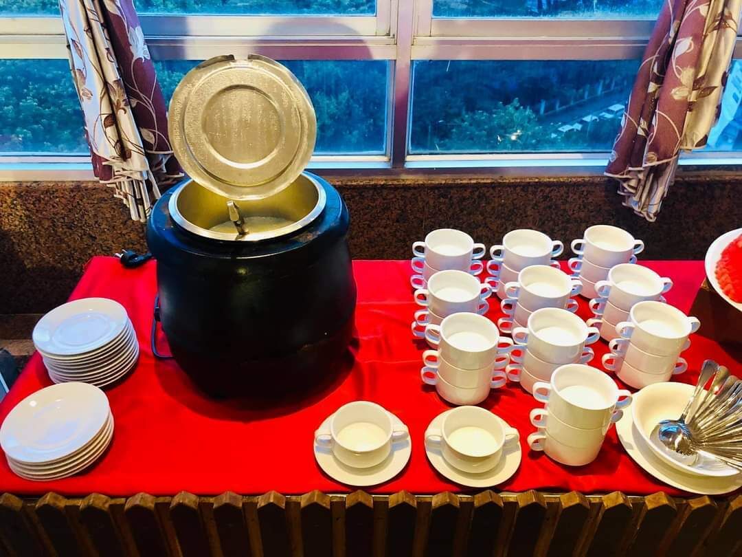 Montaje de bufé con un electrodoméstico negro grande, varias tazas y platos blancos, y un mantel rojo.
