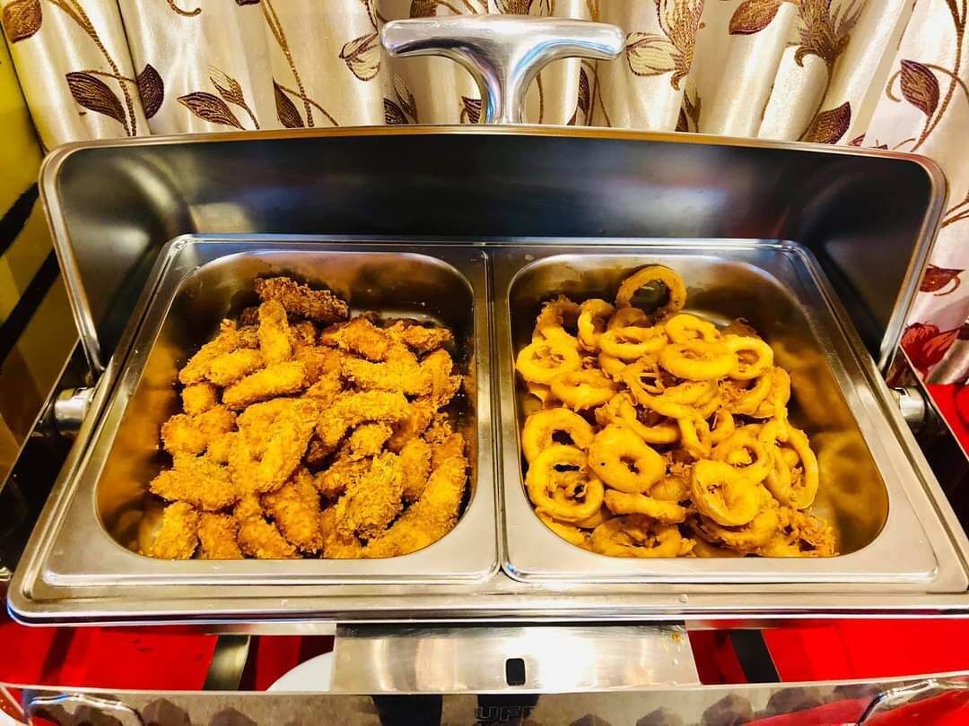 Buffet com duas travessas de comida frita, uma com frango à milanesa e outra com anéis de cebola.