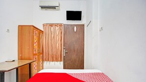 Een slaapkamer met een bed, een houten garderobe, een klein tafeltje, een aan de muur bevestigde televisie en een airconditioning.