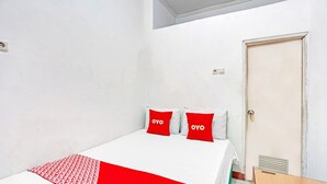 Een slaapkamer met een bed, twee rode kussens met de tekst 'OYO', een witte spreidek en een witte muur.