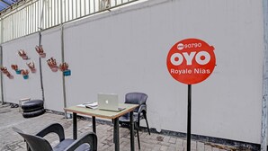 Een tafel met een laptop, twee stoelen en een bord met 'OYO Royale Nias' op een witte muur.