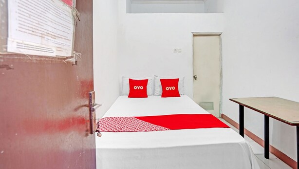 Een kleine, schone kamer met een bed, een bureau en een deur.