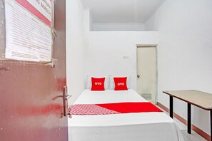 A small, clean room with a bed, a desk, and a door. - OYO 90790 Royale Nias (Surabaya)