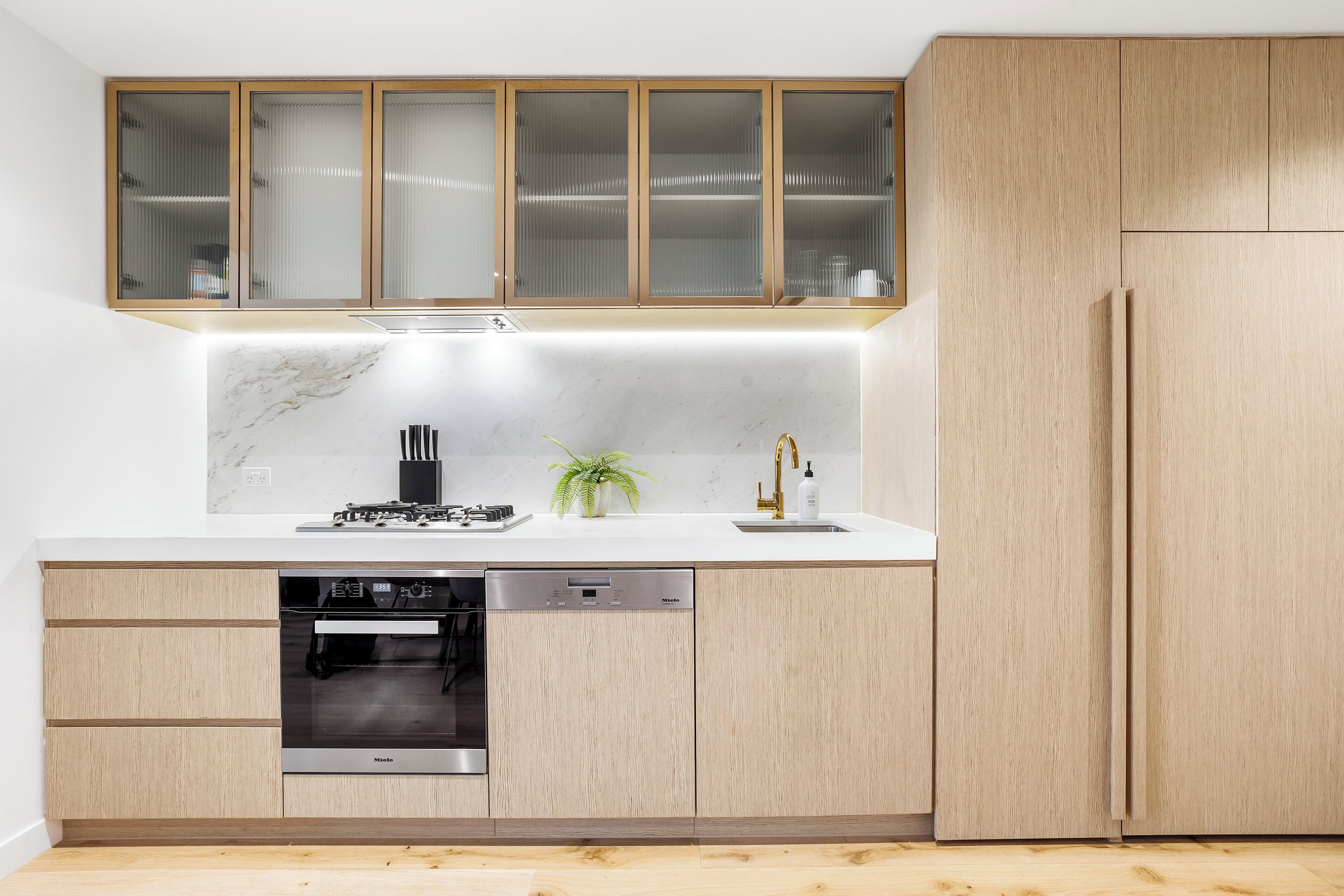 A modern kitchen with wooden cabinets, a built-in dishwasher, and a marble backsplash.