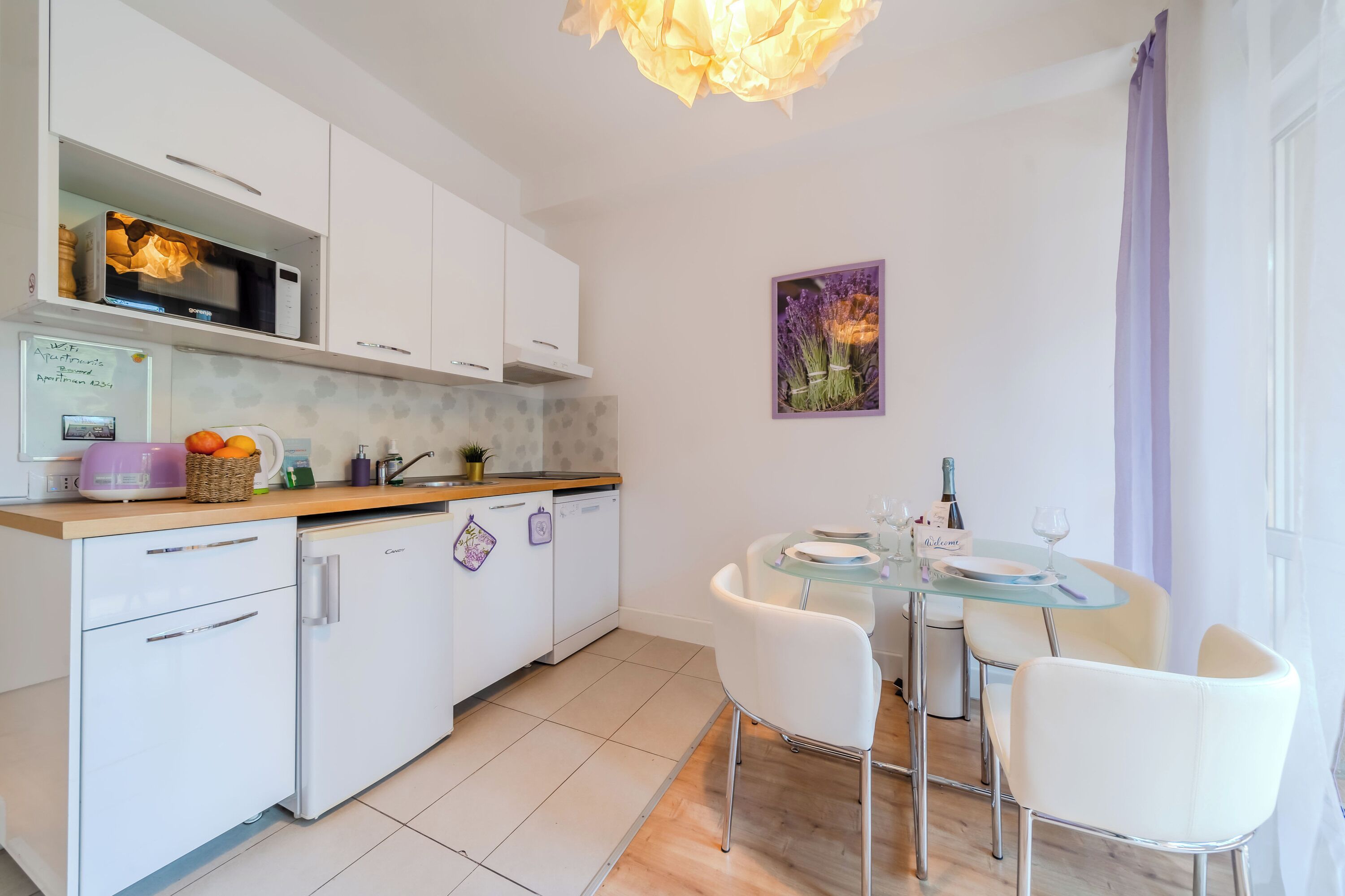 A modern kitchen with white cabinets, a microwave, and a dining area with a glass table and white chairs.