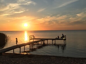 Um pôr do sol sobre um mar calmo, com um cais de madeira que se estende na água.