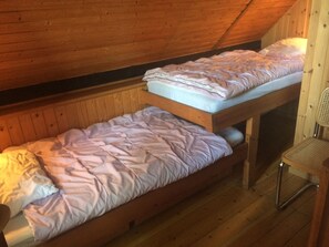 Uma pequena cabana de madeira com duas beliches, uma cadeira e teto inclinado.