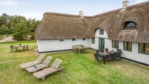 A thatched-roof cottage with a grassy yard, a dining table, and lounge chairs. - "Wandrath" - 2km from the sea by Interhome (Blåvand)