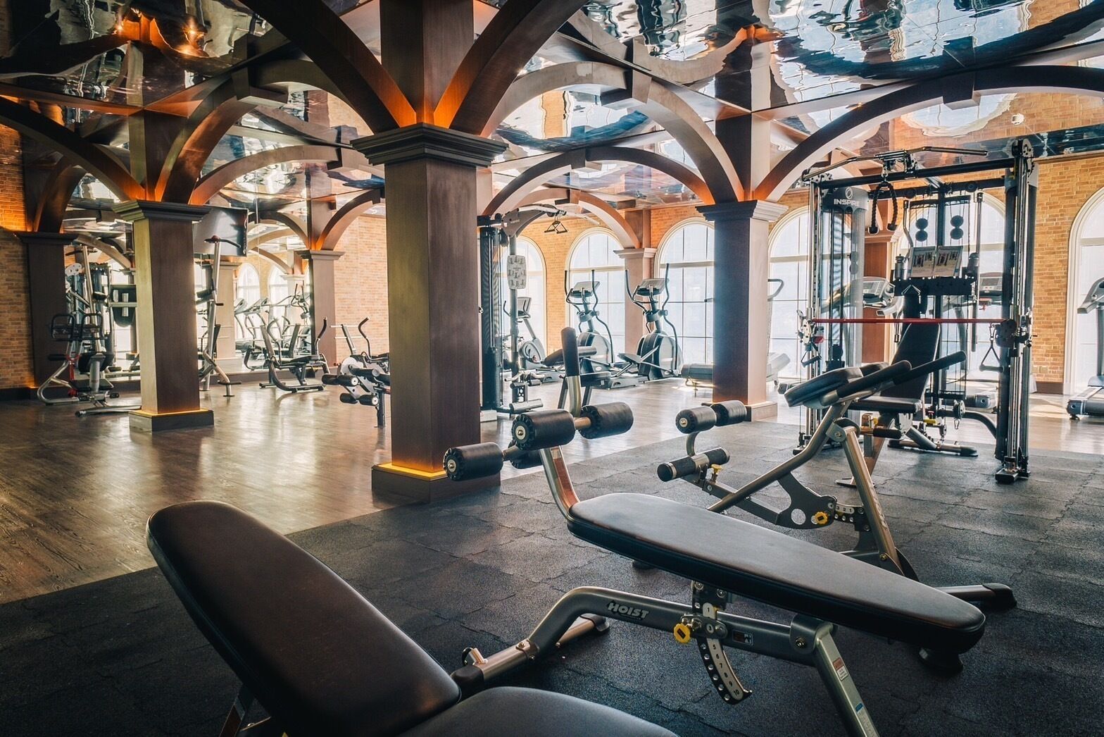 A spacious gym with various exercise equipment, large windows, and a high ceiling with exposed beams.
