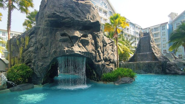 Una piscina con cascata, circondata da formazioni rocciose e palme.