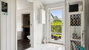 A bathroom with a toilet, a sink, and a shower area. There is a white door leading to a balcony with potted plants and a view of greenery.