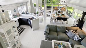 A modern kitchen with a central island, a dining area with a table and chairs, a cozy seating area with a sofa, and large windows offering a view of the outdoors.