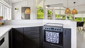 A modern kitchen with a black stove, white cabinetry, and large windows offering a view of greenery.