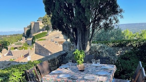 A table set outdoors with a view of a historic town and a large tree. - Village house in Ménerbes with a swimming pool and a dramatic view  (Ménerbes)