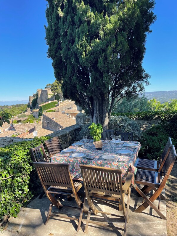 A table set outdoors with a view of a historic town and a large tree.