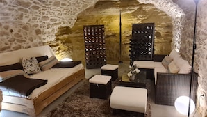 A cozy room with a stone wall, a wooden sofa, a black ottoman, a wicker chair, and a wine rack. - Village house in Ménerbes with a swimming pool and a dramatic view  (Ménerbes)