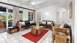 A spacious living area with a glass coffee table, two sofas, wicker furniture, and a ceiling fan.