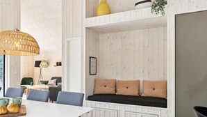 Un intérieur moderne avec un mur en bois peint en blanc, un coin repas avec une table blanche et des chaises bleues, un grand luminaire en fibres tressées et un banc intégré agrémenté de coussins.