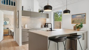 Une cuisine moderne dotée d’un grand îlot central, de luminaires suspendus et offrant une vue sur l’extérieur.