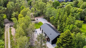 Une maison moderne dotée d’une grande terrasse, entourée d’une forêt dense et offrant une vue sur l’eau.
